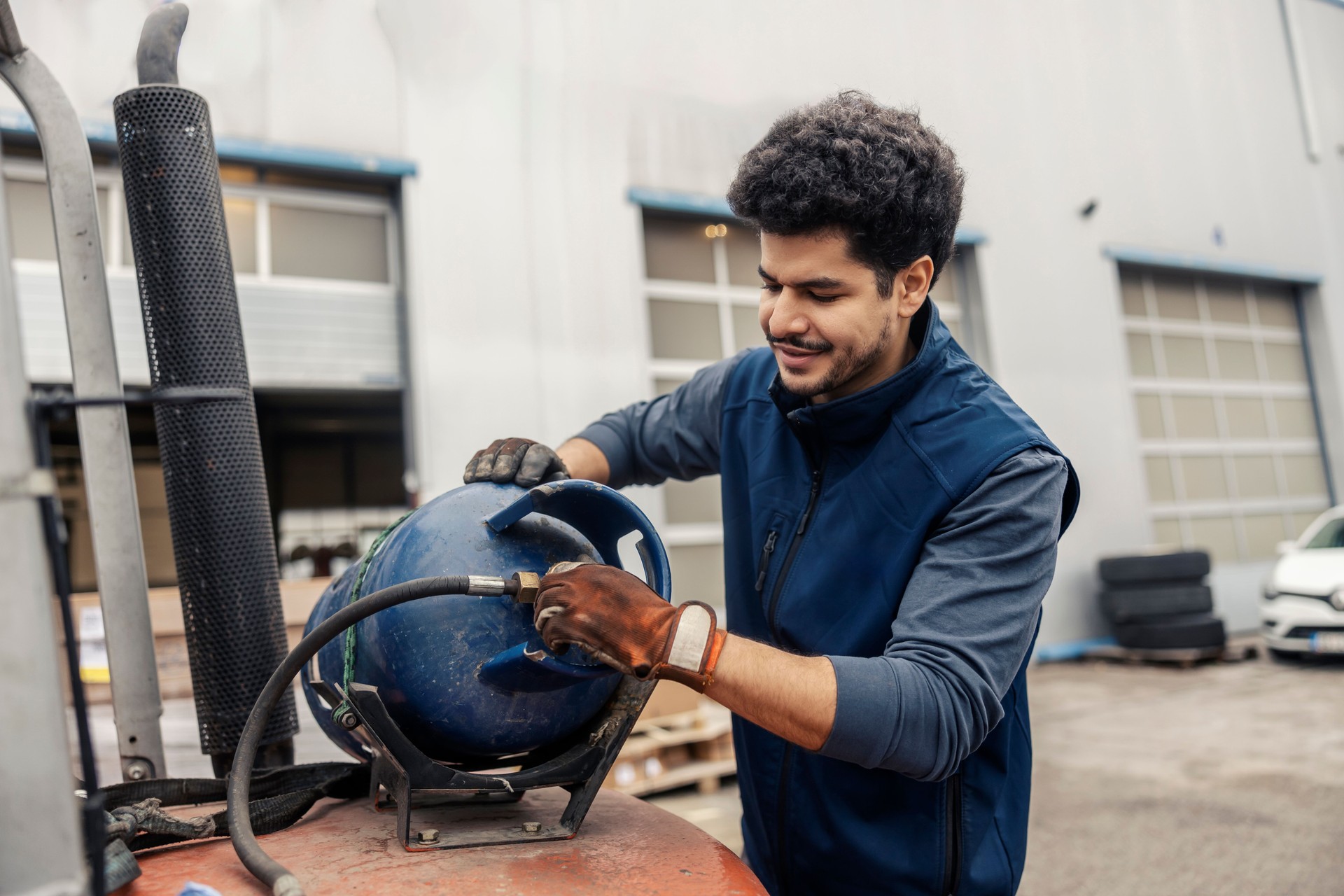 Multicultural blue collar worker attaching gas cylinder on forklift at export firm.